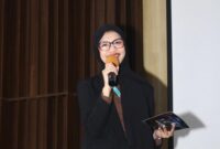 Foto: Asri Pratiwi Tenggara pembawa acara memandu jalannya kegiatan dengan penuh semangat di atas panggung. Dengan mengenakan busana formal, ia tampak percaya diri menyampaikan informasi kepada audiens yang hadir, menciptakan suasana acara yang hangat dan interaktif.