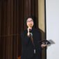 Foto: Asri Pratiwi Tenggara pembawa acara memandu jalannya kegiatan dengan penuh semangat di atas panggung. Dengan mengenakan busana formal, ia tampak percaya diri menyampaikan informasi kepada audiens yang hadir, menciptakan suasana acara yang hangat dan interaktif.