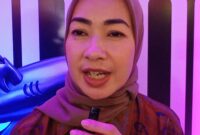 Foto: Alia Rohali terlihat berdiri di depan latar bertema Flying Fish Alumni sambil memegang mikrofon kecil.