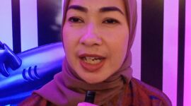 Foto: Alia Rohali terlihat berdiri di depan latar bertema Flying Fish Alumni sambil memegang mikrofon kecil.