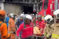 Foto: Petugas pemadam kebakaran mengevakuasi korban dari dalam gedung yang terbakar di kawasan Cempaka Baru, Kemayoran, Jakarta Pusat, Selasa (9/12/2025).
