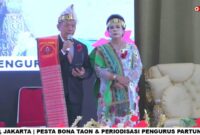 Foto: Ketua Umum terpilih Partungkoan Guru Hinombingan Silitonga se-Jabodetabek periode 2026–2030, Dr. Dikson Silitonga, menyampaikan sambutan didampingi seorang tokoh perempuan dalam balutan busana adat Batak pada acara Pesta Bona Taon dan Periodeisasi Pengurus di Sopo Marpingkir.