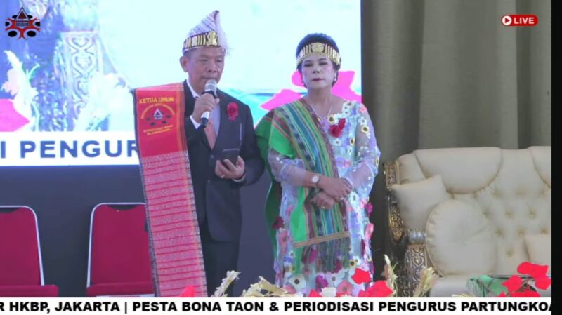 Foto: Ketua Umum terpilih Partungkoan Guru Hinombingan Silitonga se-Jabodetabek periode 2026–2030, Dr. Dikson Silitonga, menyampaikan sambutan didampingi seorang tokoh perempuan dalam balutan busana adat Batak pada acara Pesta Bona Taon dan Periodeisasi Pengurus di Sopo Marpingkir.