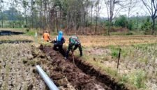 Foto: MADIUN — Seorang Babinsa bersama warga bergotong royong menggali tanah untuk pemasangan jaringan pipa irigasi perpompaan di area persawahan Desa Geger, Kecamatan Geger, Kabupaten Madiun, Sabtu (22/8/2026).