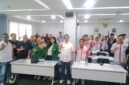 Foto: Peserta kegiatan bersama narasumber dan tamu undangan berfoto bersama dengan mengangkat tangan di ruang pertemuan.