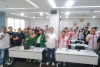 Foto: Peserta kegiatan bersama narasumber dan tamu undangan berfoto bersama dengan mengangkat tangan di ruang pertemuan.