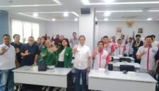 Foto: Peserta kegiatan bersama narasumber dan tamu undangan berfoto bersama dengan mengangkat tangan di ruang pertemuan.