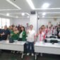 Foto: Peserta kegiatan bersama narasumber dan tamu undangan berfoto bersama dengan mengangkat tangan di ruang pertemuan.